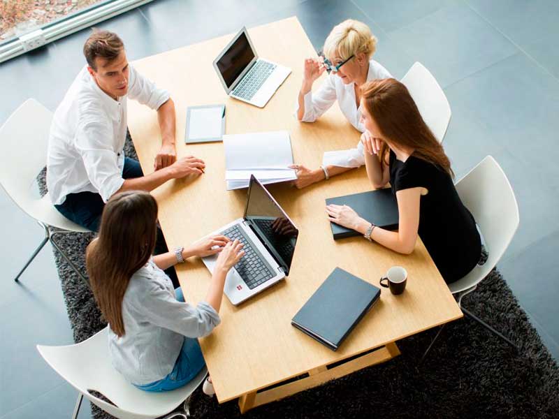 Grupo de personas reunidas alrededor de una mesa trabajando con portátiles y documentos.